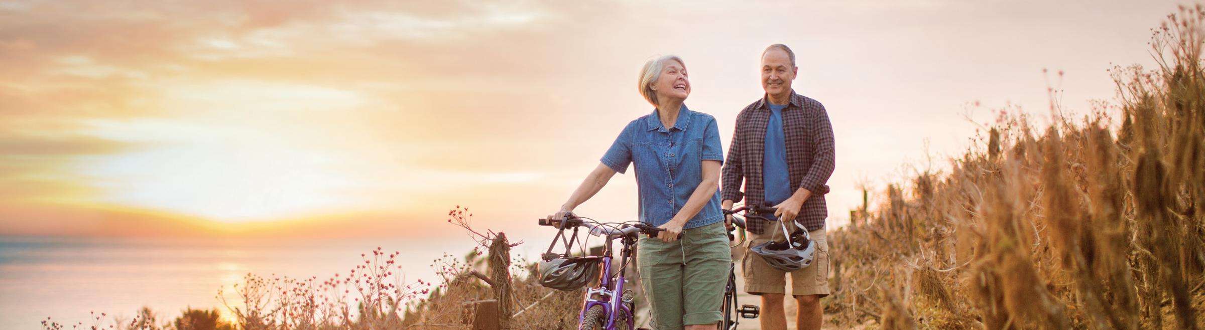 Older couple walking their bikes along coastline