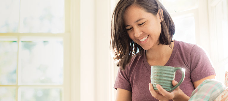 Woman drinking coffee and smiling in bright living room