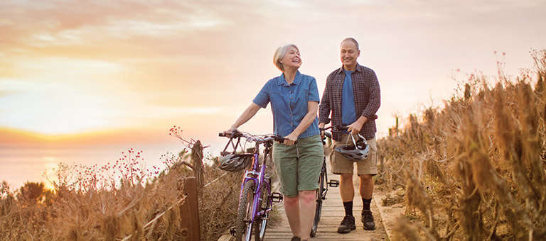 Older couple walking their bikes along coastline