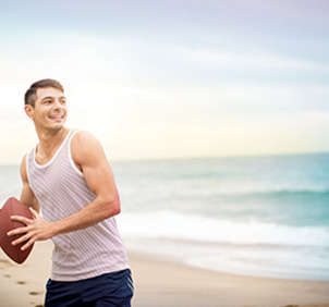 Man in tank top throwing football on beach